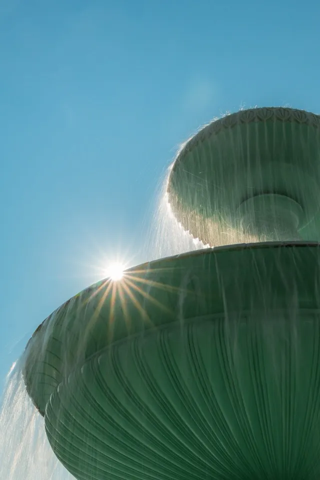 Une fontaine dont l'eau déborde en rideaux, le soleil en étoile derrière