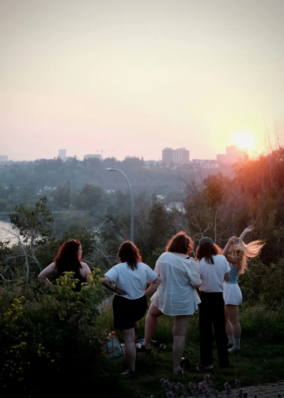 Un groupe de jeunes de dos face à la ville, au soir